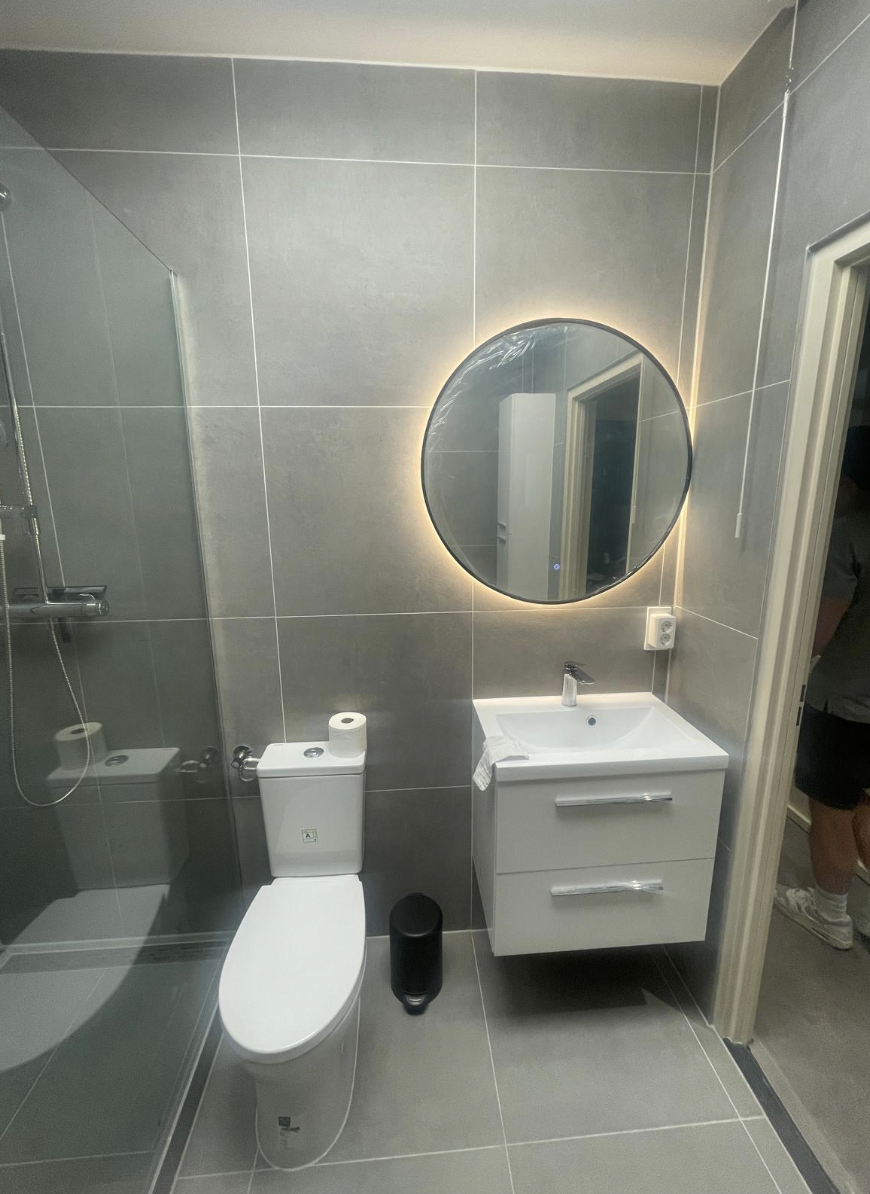 Badkamer met ronde spiegelverlichting, hangtoilet en wit meubel